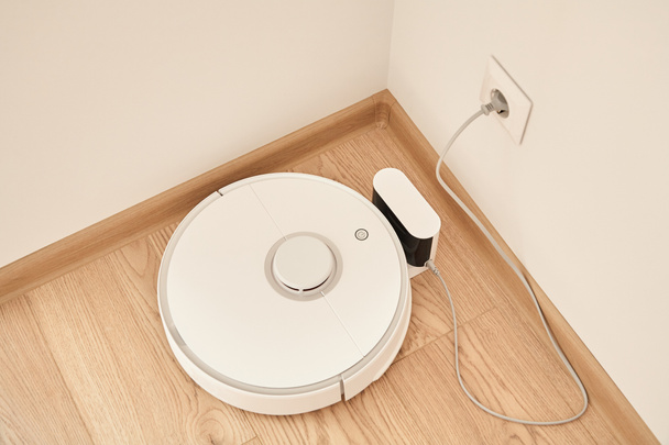 top view of modern robotic vacuum cleaner near power socket on wall  - Photo, Image