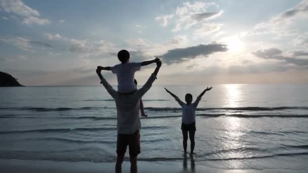 Szczęśliwa azjatycka rodzina na wakacjach Syn na plecach ojcowie i mama Otwórz ramiona grając samolot razem na plaży. Tło zachód słońca w morzu. Relaks Koncepcja wakacje i podróże. Zwolniony ruch - Materiał filmowy, wideo