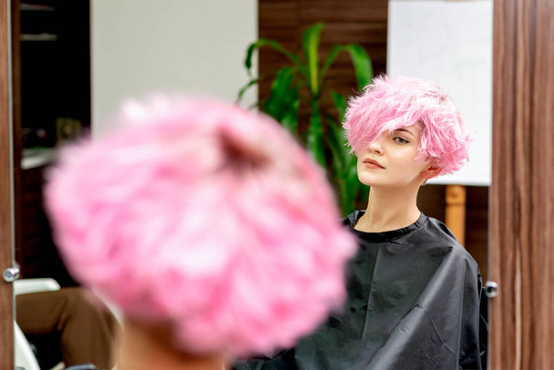 Woman with pink hair looking in the mirror at hair salon. - Photo, Image
