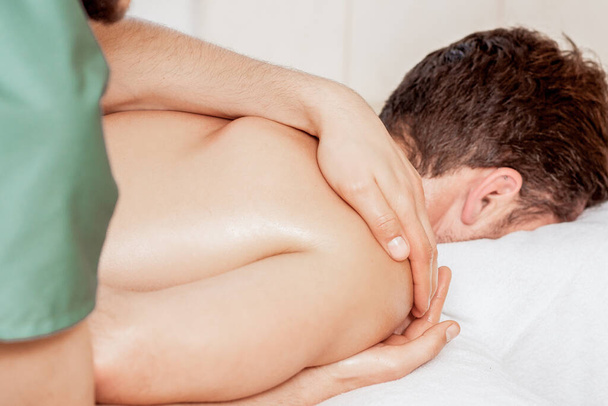 Zbliżenie rąk masażysty wykonujących masaż wellness na ramieniu mężczyzny w spa. - Zdjęcie, obraz
