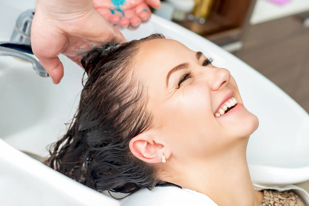 Женщина принимает мытье волос в раковине смеясь в парикмахерской
. - Фото, изображение