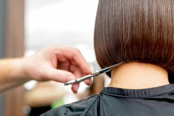 Vista posterior de la mano peluquería está cortando puntas de pelo de mujer peinado corto en el salón de belleza
. - Foto, Imagen