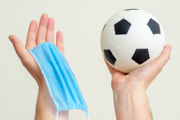 Labdarúgás labda és orvosi maszk férfi kezekben fel fehér háttér. - Fotó, kép