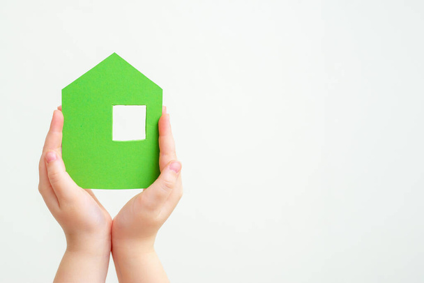 Dětské ruce drží zelený papírový dům na bílém pozadí. - Fotografie, Obrázek