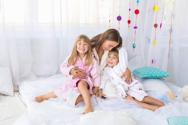 Young woman playing on the bed with the two daughters at home. Stay home and family concept. - Photo, Image