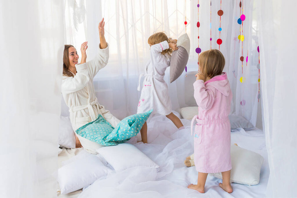 Giovane donna divertirsi con i bambini che giocano con cuscini sul letto in camera da letto. Rimani a casa e concetto di famiglia
. - Foto, immagini