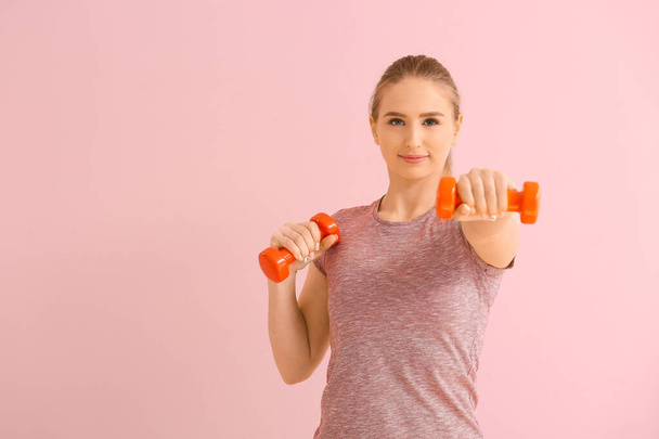 Sportieve jonge vrouw training met halters op kleur achtergrond - Foto, afbeelding
