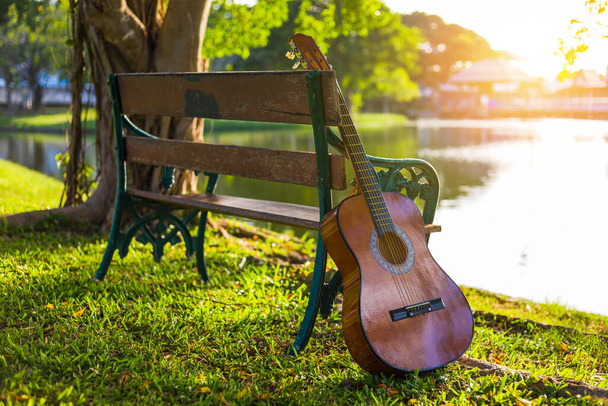 guitar acoustic standing beside wood bence in the parks and light of sunset. - Valokuva, kuva