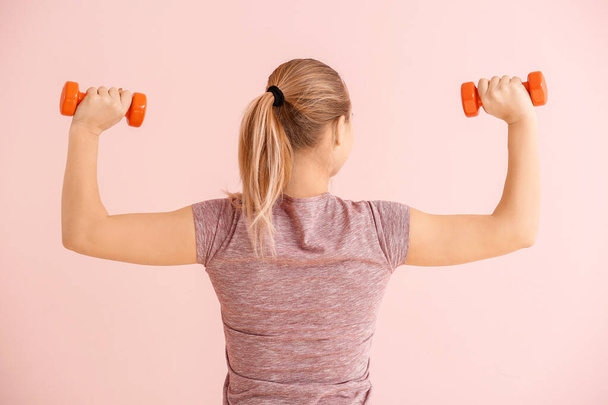 Sportieve jonge vrouw training met halters op kleur achtergrond - Foto, afbeelding