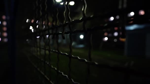 Metal mesh. Empty basketball court at night in the lights of lanterns. View of an outdoor basketball court through a metal mesh. Street sport. Jail. Conclusion. Closed area. - Footage, Video