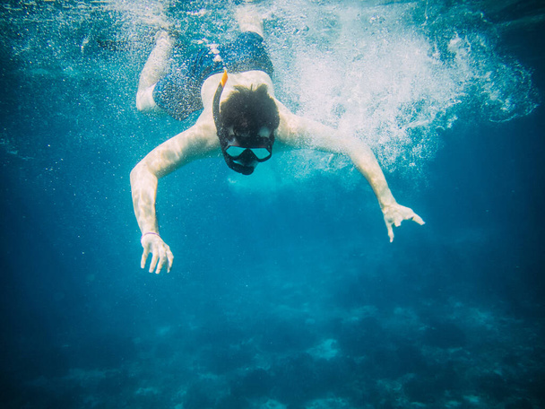Underwater view of a young diver man swimming under blue sea under the surface with snorkelling mask for summer vacation at Similan islands, Andaman sea, Phang Nga near Phuket nad Krabi in Thailand. - Foto, Imagem