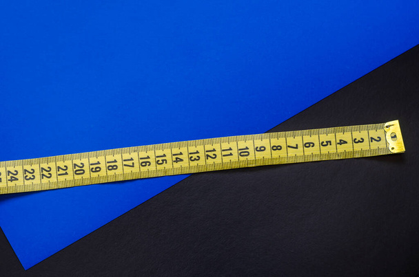 Measuring tape on a two-color background. Yellow tailor meter on a black and blue background. Multitask background. Place for text. View from above. - Photo, Image