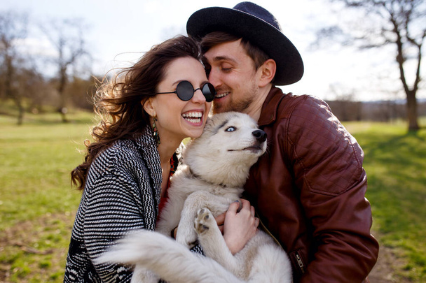 Bild eines Paares umarmt seinen Husky-Hund im Park, auf einer schönen Frühlingslandschaft Hintergrund. - Foto, Bild