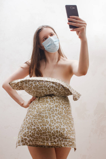 Kobieta w masce medycznej, sukienka poduszki podejmowania selfie zdjęcie na telefon komórkowy dla szalonych Wyzwanie poduszki ze względu na pobyt w domu izolacji. Dziewczyna od mody. Wyzwanie poduszki ze względu na izolację domu.  - Zdjęcie, obraz