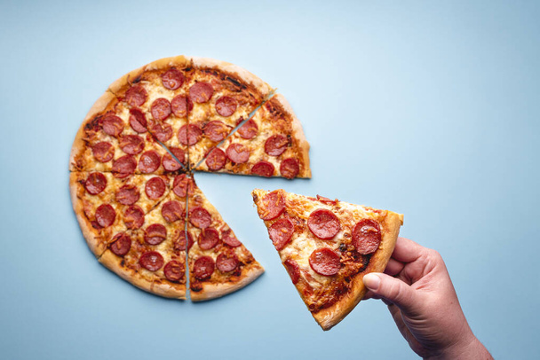 Vue de dessus avec la main d'une femme prenant une tranche d'une pizza pepperoni. Délicieuse pizza salami maison vue sur le dessus. Restauration rapide maison-cuit
 - Photo, image