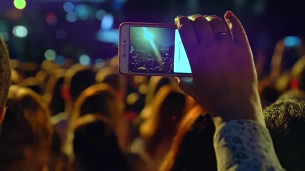 Gratis concert. Gelukkige mensen kijken naar een geweldig muzikaal concert. Vrolijke fans springen en steken hun handen op. Fans filmen een concert op een smartphone. Live concert. - Video