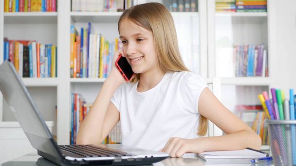 Kid Studying Browsing Internet on Laptop while Talking Smartphone, Child Learning, Writing in Library, Schoolgirl Chatting with Teacher on Phone from Home due to Coronavirus Pandemic Crisis, Children Homeschooling, Online Education - Foto, imagen