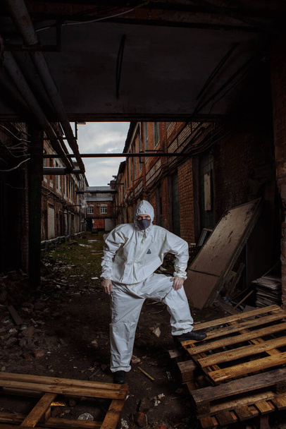 muž v ochranném obleku, šedé lékařské masce a latexových rukavicích během pandemie koronaviru COVID-19 v troskách města - Fotografie, Obrázek