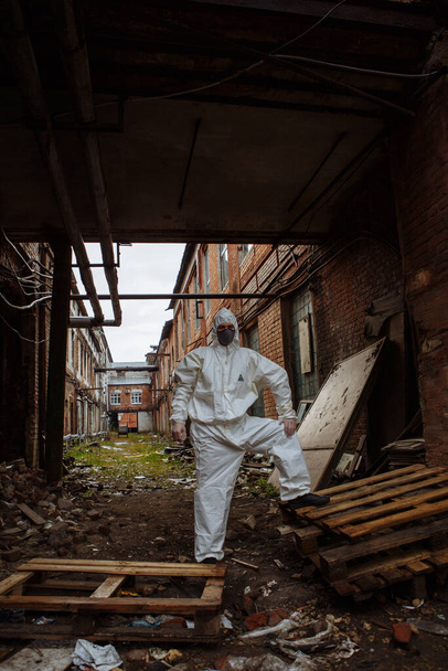 человек в защитном костюме, серой медицинской маске и латексных перчатках во время пандемии коронавируса COVID-19 в руинах города
 - Фото, изображение