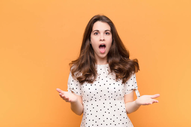 young pretty woman feeling extremely shocked and surprised, anxious and panicking, with a stressed and horrified look against orange wall - Fotó, kép