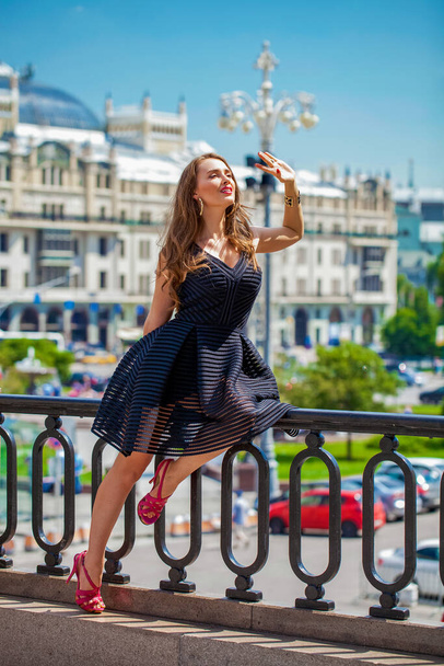 Portrait in full growth, Young beautiful brunette woman in black dress posing outdoors in sunny weather - Фото, изображение