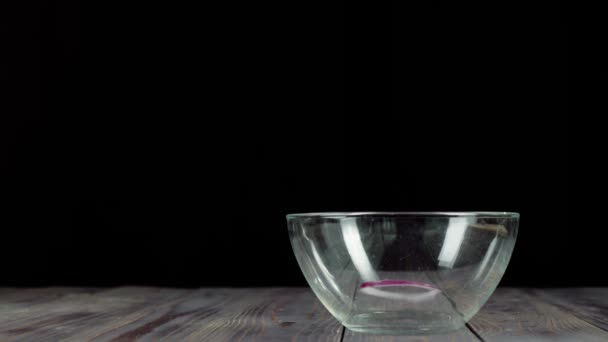 A szeletelt lila hagyma leesik egy üres üvegtálba egy fa asztalon. A friss nyári saláta elkészítése salátából, cseresznyés paradicsomból, uborkából és hagymából. Középső lövés. 4K - Felvétel, videó