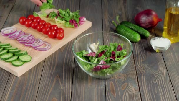 Nyári saláta. A profi séf friss zöld és sárgarépa salátát tölt üvegtálba. A friss nyári saláta elkészítése salátából, cseresznyés paradicsomból, uborkából és hagymából. Középső lövés. 4K - Felvétel, videó
