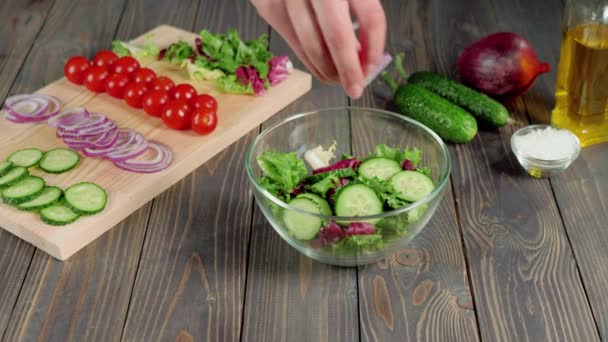 Nyári saláta. Professzionális szakács önti szeletelt lila hagyma üvegtálba. A friss nyári saláta elkészítése salátából, cseresznyés paradicsomból, uborkából és hagymából. Középső lövés. 4K - Felvétel, videó