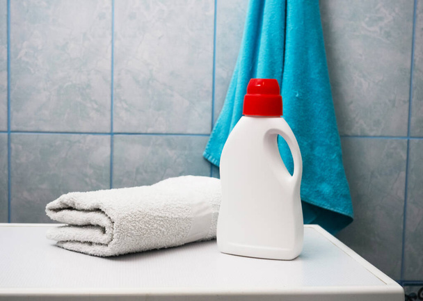 Μπουκάλι απορρυπαντικό και καθαρές πετσέτες στο πλυντήριο σε εσωτερικούς χώρους, χώρος για κείμενο. Ημέρα πλυντηρίου. - Φωτογραφία, εικόνα