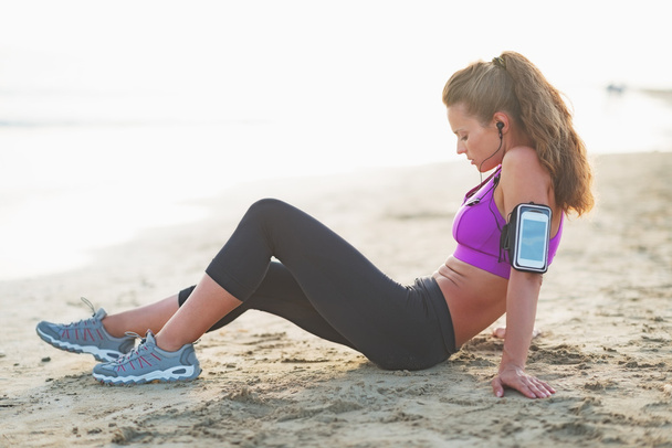 Relaxed fitness young woman in headphones sitting on beach - Foto, immagini
