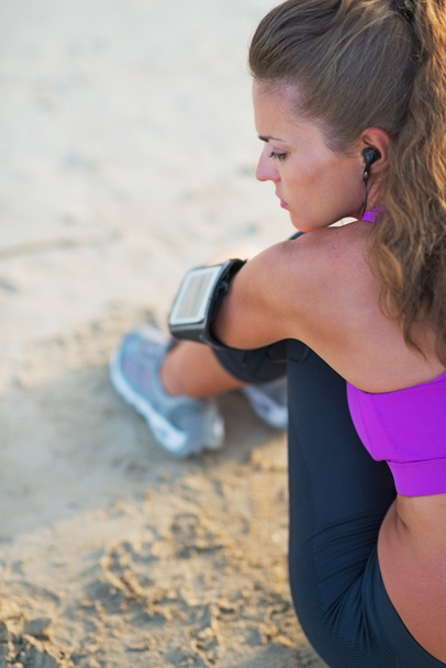 Fitness young woman in headphones sitting on beach - Valokuva, kuva