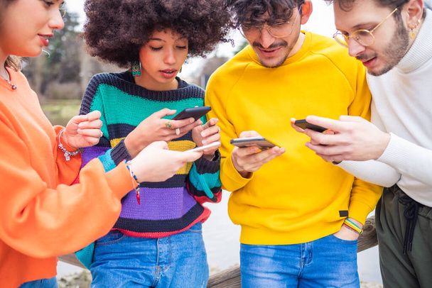 Grupo de cuatro personas amigos al aire libre utilizando el teléfono inteligente - uso excesivo, búsqueda, concepto de compras
 - Foto, Imagen