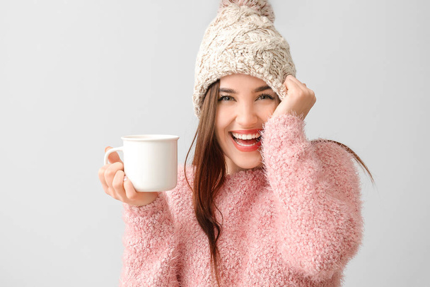 Όμορφη ευτυχισμένη νεαρή γυναίκα με φλιτζάνι ζεστό κακάο στο φως φόντο - Φωτογραφία, εικόνα