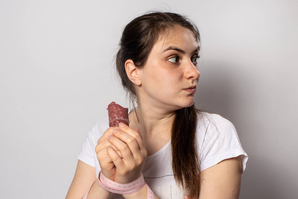 Женщина с копченой колбасой и сантиметровой лентой на руках. Нарушение диеты при похудении. Отказ от правильного питания, вредных высококалорийных продуктов
. - Фото, изображение