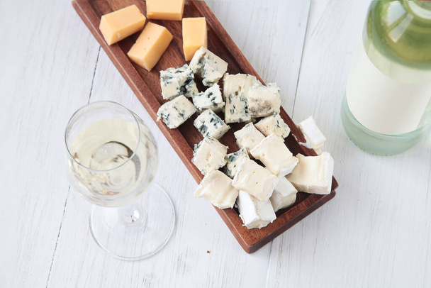 Glas witte wijn, een fles wijn en een bord kaas op een houten ondergrond - Foto, afbeelding