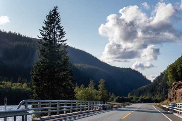Sonnige skandinavische Tagestour. Schwedische Naturlandschaft mit Autobahn. Bäume, Berge, malerische Wolken und Einfahrt - Foto, Bild