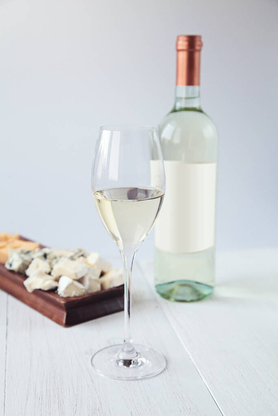 Γυαλί με λευκό κρασί στο παρασκήνιο ένα μπουκάλι και τυρί - Φωτογραφία, εικόνα
