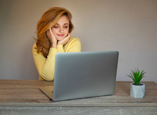 Egy fiatal nő online dolgozik. Laptopos lány. Mosolygó nő sárga kardigánban. - Fotó, kép