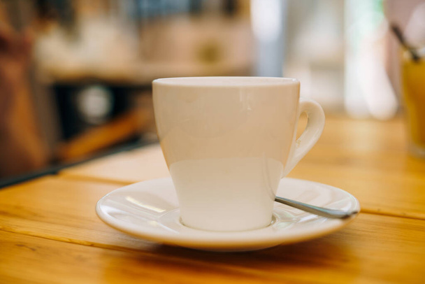 Белая чашка с кофе на тарелке. Горячий эспрессо в чашке на деревянном столе. Эспрессо на завтрак в кафе
 - Фото, изображение