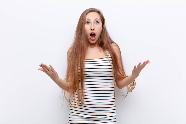 yound blonde woman open-mouthed and amazed, shocked and astonished with an unbelievable surprise against white wall - 写真・画像