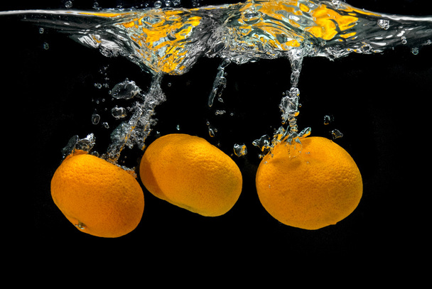 Fresh tangerines dropped into water with bubbles on black - Фото, изображение