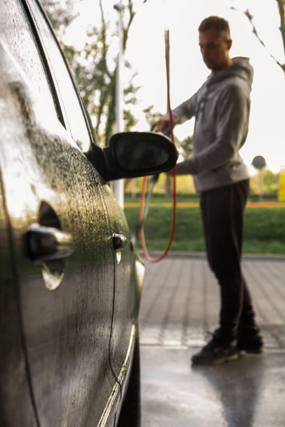 Ένας άνθρωπος πλένει ένα αυτοκίνητο σε ένα πλυντήριο αυτοκινήτων self-service. - Φωτογραφία, εικόνα