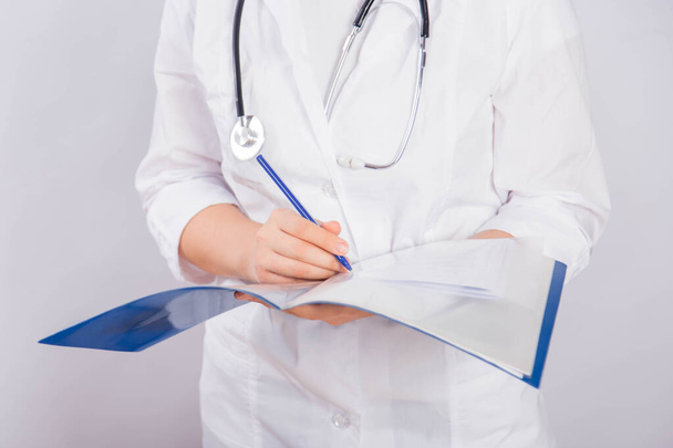 Le mani del medico in un cappotto bianco tengono una cartella e compilano un documento medico da vicino isolato su uno sfondo bianco
. - Foto, immagini