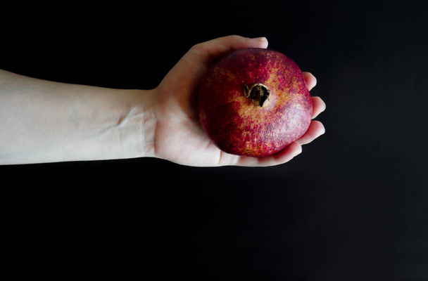 ripe pomegranate in the hands of a girl on a black background with place for your text - Fotoğraf, Görsel