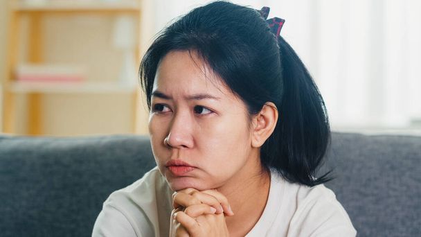 Depressief huilen Aziatische zakenvrouw gestrest met hoofdpijn zittend op de bank in de woonkamer thuis wanneer sociale afstand verblijf thuis en self quarantaine tijd, coronavirus concept. - Foto, afbeelding