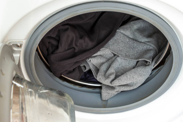 Lavage dans une machine à laver. Tambour de machine à laver ouvert avec des vêtements en coton noir et gris préparés pour le lavage close-up
 - Photo, image