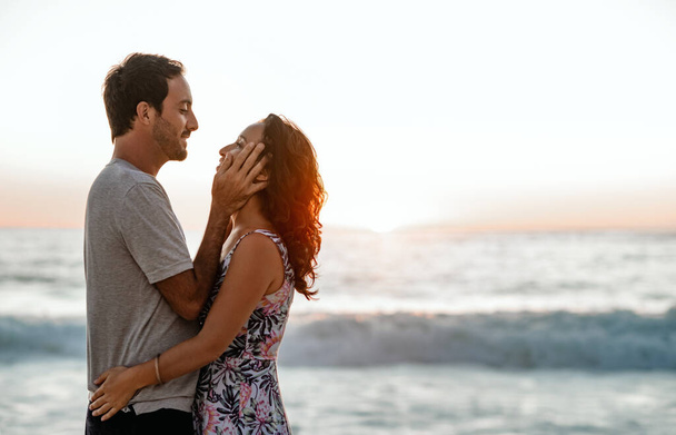 Affectionate young couple staring into each other's eyes while enjoying a sunset together at the beach - Foto, Imagem