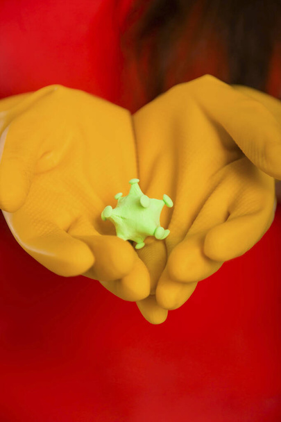Großaufnahme Putzfrau Hände mit Coronavirus-Modell auf gelben Handschuhen. Konzeptkunst der Reinigung der Räumlichkeiten und der Prävention von Viruserkrankungen. - Foto, Bild