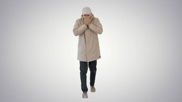 Man in winter outfit walking and coughing on gradient background. - Фото, зображення