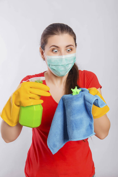 A young woman in a mask and gloves holds a spray bottle and a rag with a model of coronavirus. Concept art for cleaning the premises and the prevention of viral diseases. - Foto, imagen